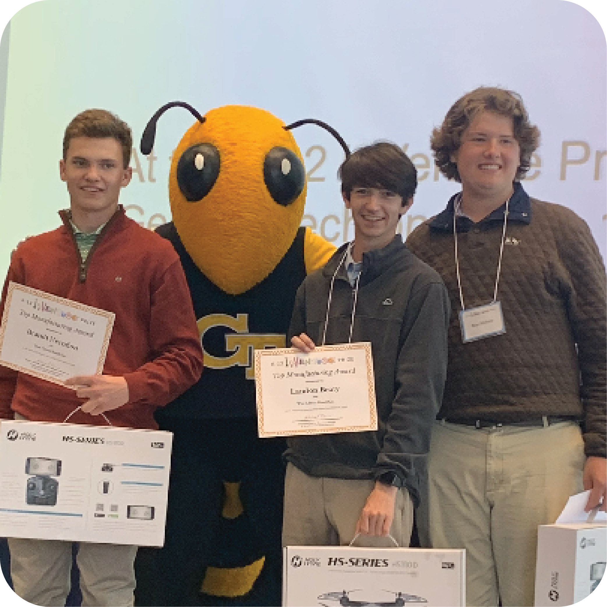 Three smiling students holding prizes and standing next to Buzz (Georgia Tech's yellowjacket mascot).